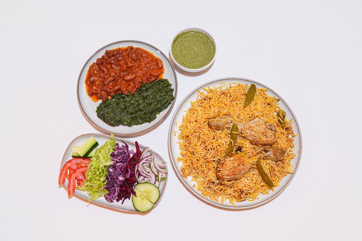 Plates of biryani with chicken, chutneys, and fresh salad vegetables on a white background.